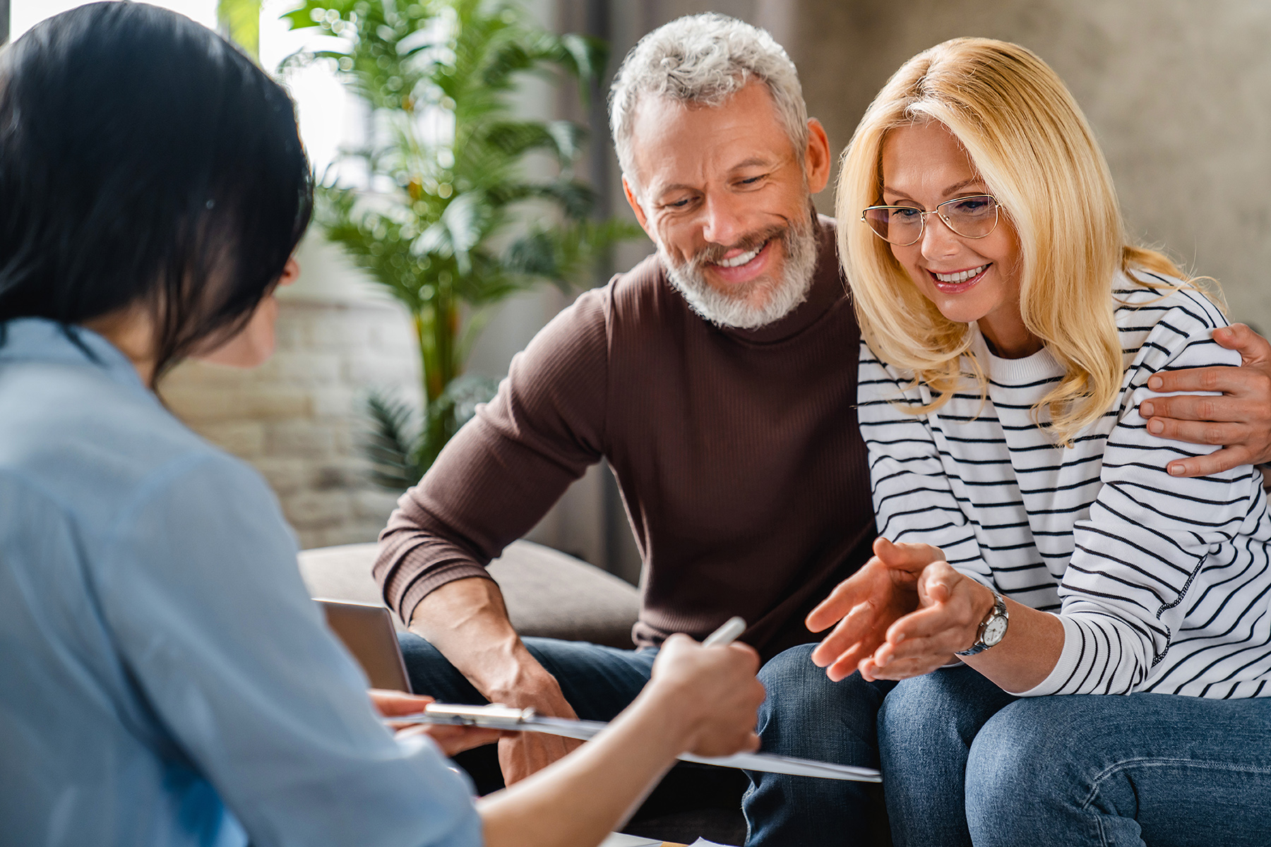 Estate agent or financial adviser showing terms of contract to happy couple on notepad