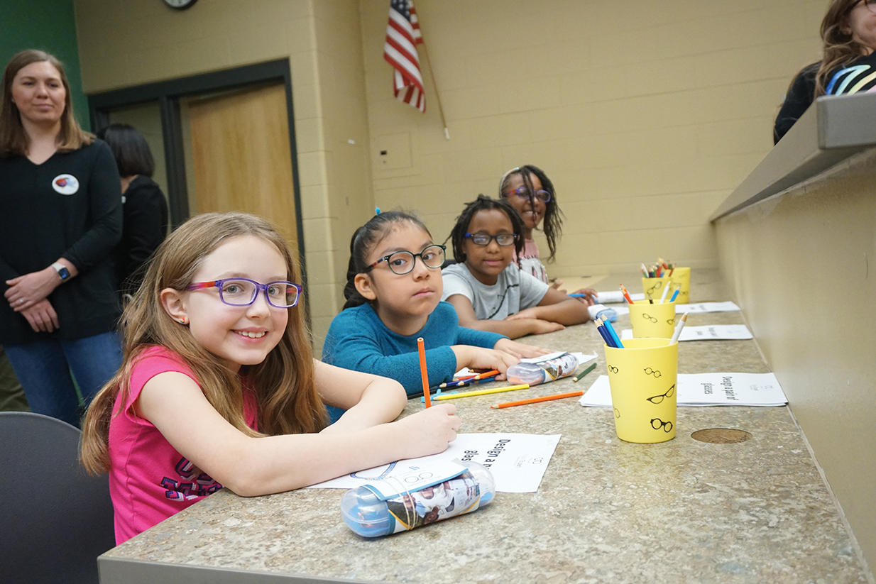 Girls in glasses sit in a classroom.